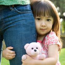 Three year old girl clinging to mother's leg