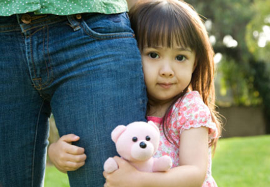 Three year old girl clinging to mother's leg